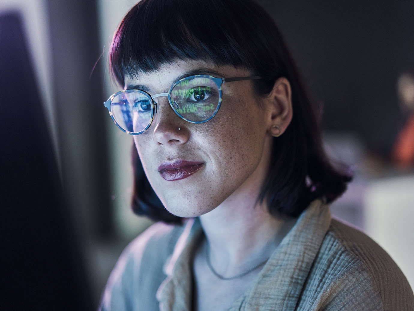 A woman with short hair and glasses looking at a laptop screen
