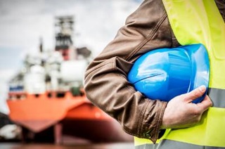 A man in a safety jacket with a helmet in hand