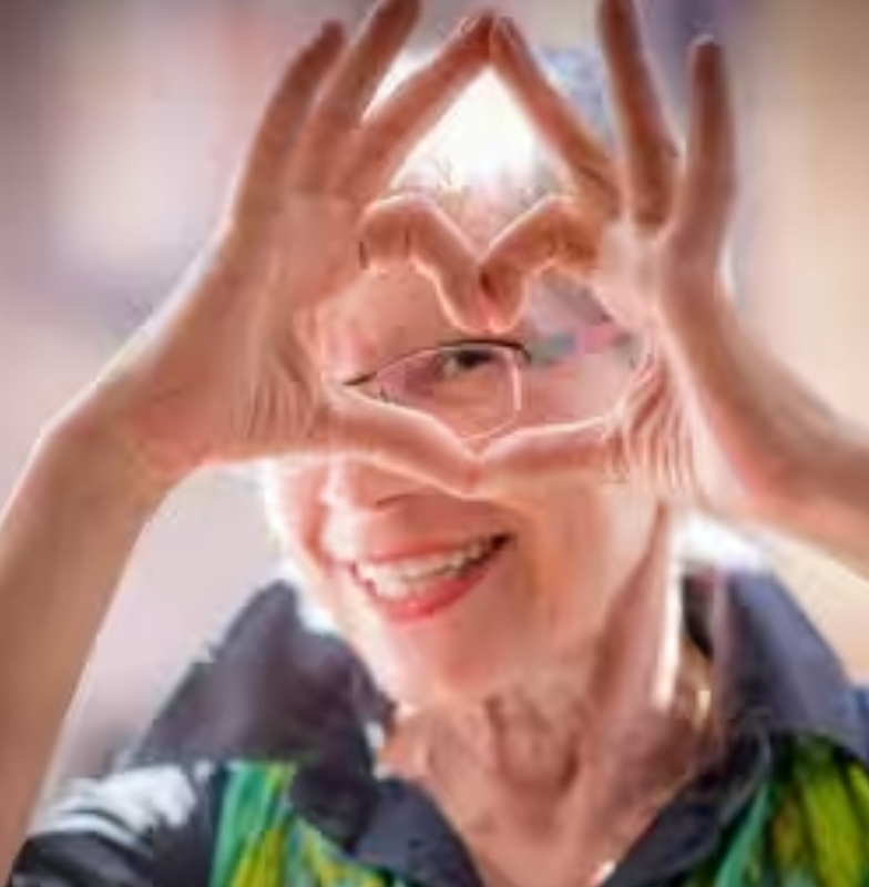 An elderly lady smiling and joining her hands to form a heart