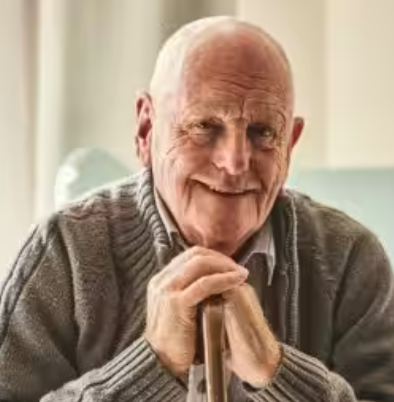 An elderly man holding a cane and smiling