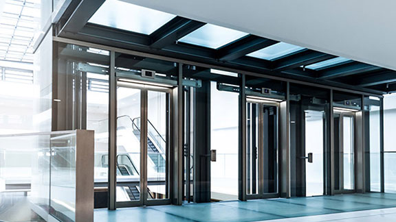 A brightly lit lobby in a building, with glass doors leading to escalators