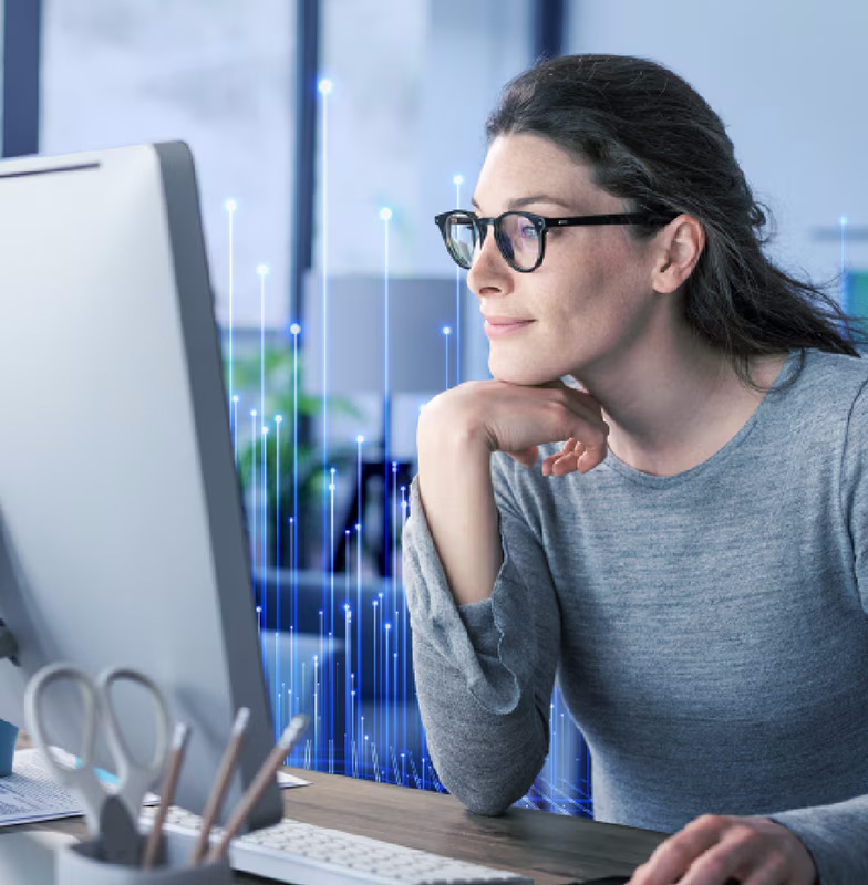 Woman working on her laptop at the edge of a room against a backdrop of skyscrapers