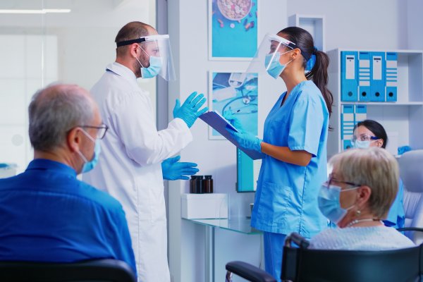 Two medical staff talking in a consultation room with patients sitting